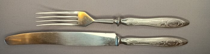 Gammalt bestickset med kniv och gaffel, silverfärgat och dekorerade med blommönster, från en loppisfyndad samling.