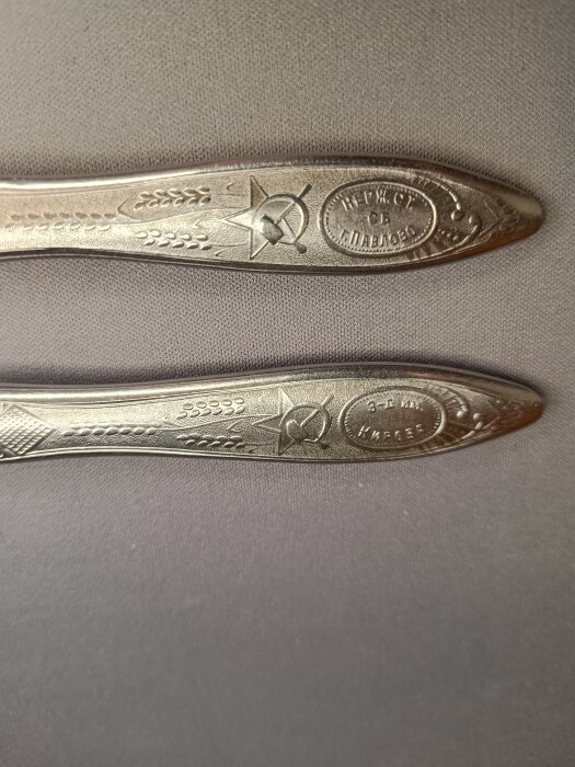 Två dekorerade bestick med ryska inskriptioner och symboler, liggande på en grå yta.