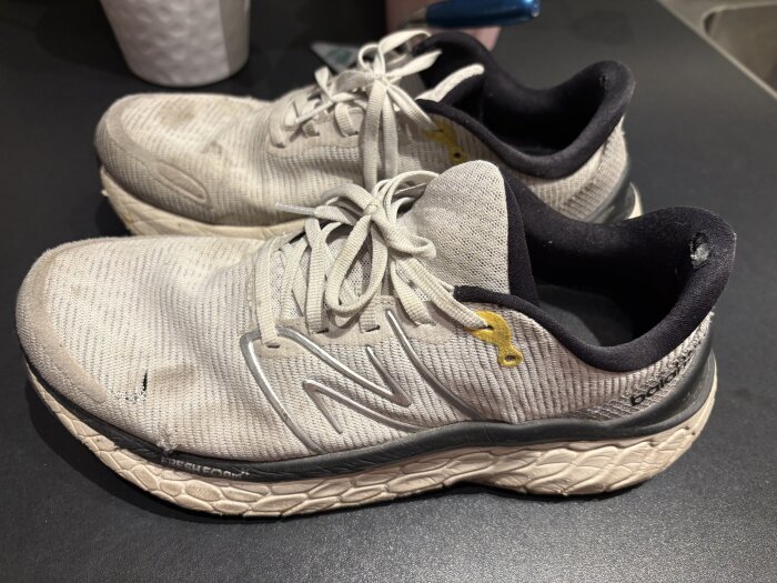 Vita löparskor med slitna detaljer på svarta bordet, med märkeslogo på sidan och mjuk dämpad sula.