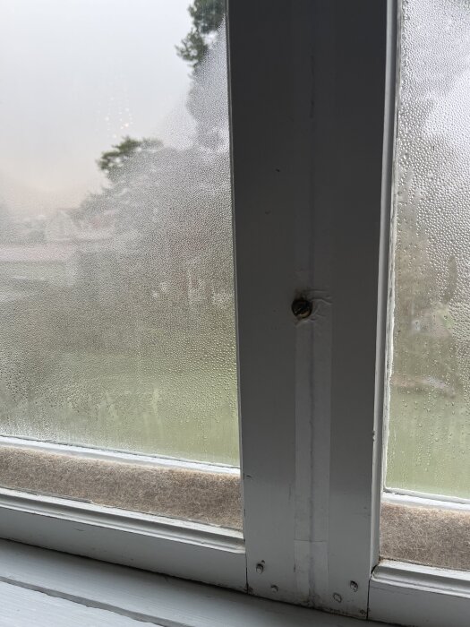 Fönster med synlig kondens och fuktdroppar på glaset i ett äldre hus, indikerar problem med isolering och ventilation.