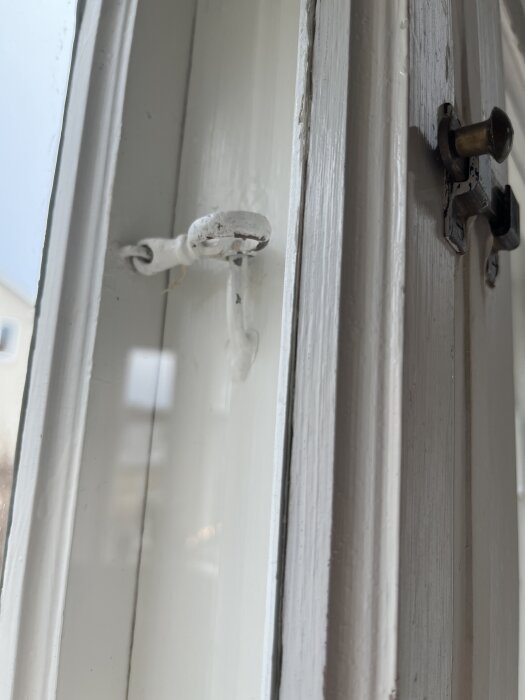 Fönsterhakar i närbild på ett vitmålat fönster inomhus.