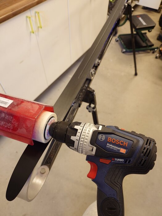 Bosch skruvdragare används för att valla skidans undersida med en röd borste i en verkstadsmiljö.
