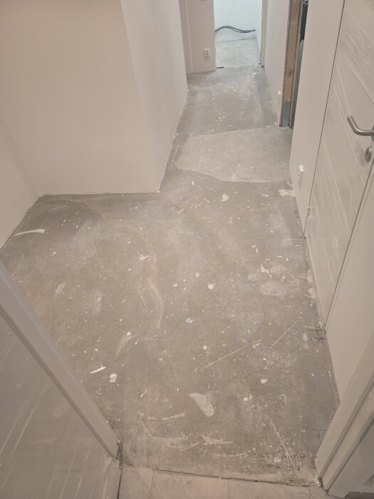 Bilden visar ett nyligen flytspacklat golv i en korridor och ett förråd, med märkbara nivåskillnader och ojämnheter i ytan.