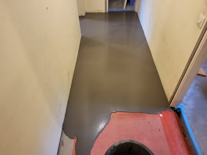 Flytspacklat golv i en korridor, delvis täckt med röd skyddsmatta; förberett för plattsättning.