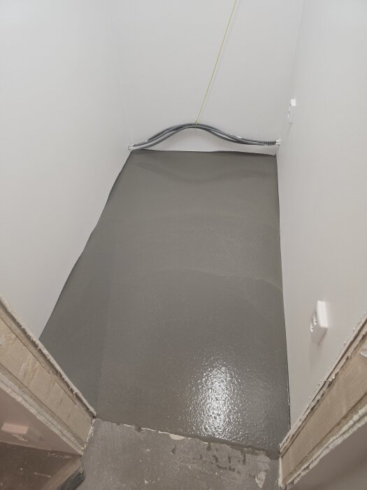 Nyligen flytspacklat golv i en vit korridor, ser slätt och jämnt ut. Förberett för kommande plattsättning.