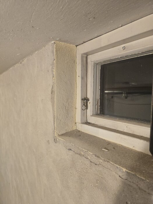 Slitet fönster med krackelerad träram och putsad murbruk runt, på insidan av en vägg före renovering.