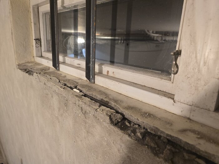 Gammalt fönster med uttorkad och krackelerad träram, murbruk har lossnat från ramen, visar nödvändigt renoveringsarbete.