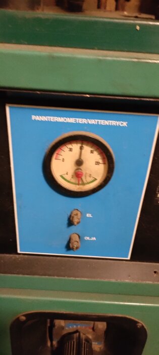 Närbild av en blå panel med texten "PANNTERMOMETER/VATTENTRYCK" och en ratt för temperaturjustering, samt två vred märkta "EL" och "OLJA".