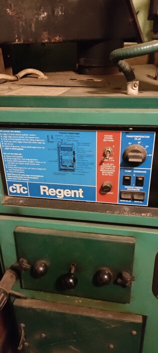 Närbild av en gammal pelletspanna med märket CTC Regent, visar olika reglage och instruktioner på en panel.