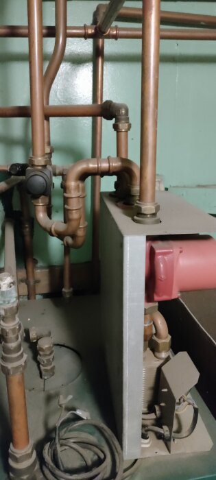 Kopparrör och reglage på pelletspannan i ett pannrum, med några oisolerade delar och elkablar i förgrunden.