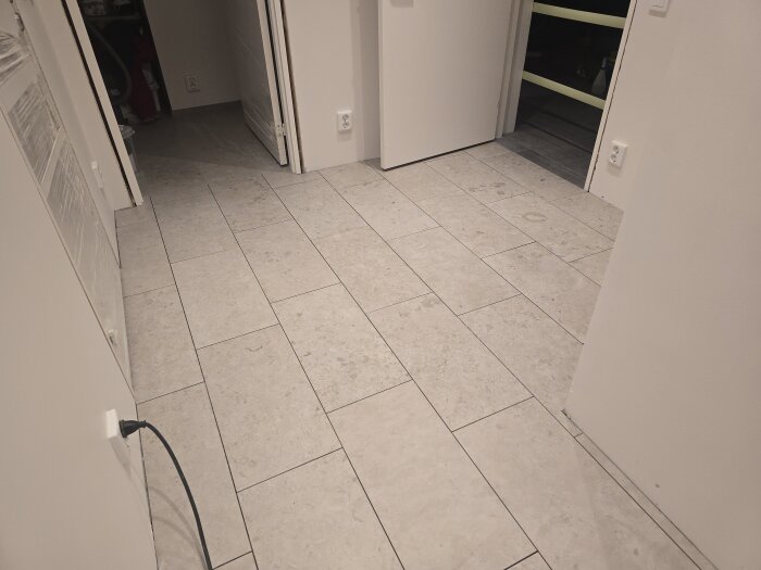 Nyinstallerat stengolv i korridor med ljusa, rektangulära plattor. Dörrar och vägguttag syns längs sidorna i rummet.