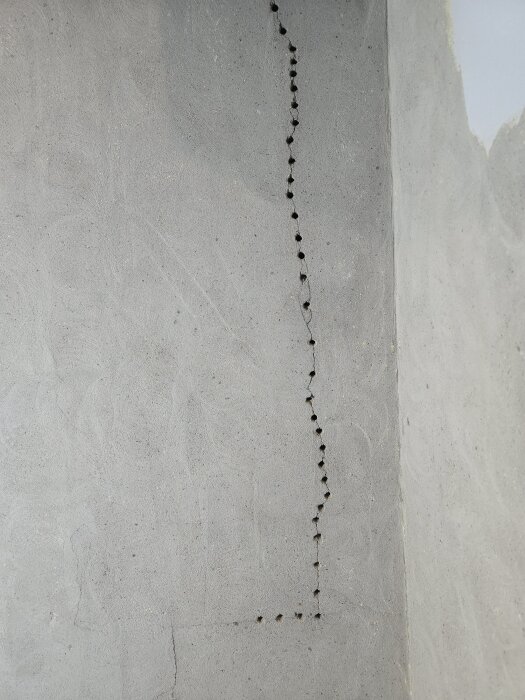 En vägg med borrade hål i ett raka linjer, förberett för spricklagning och eldragning.