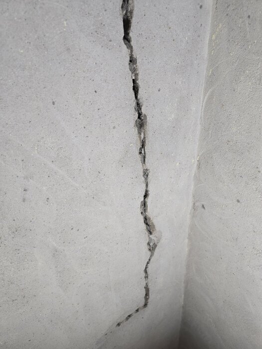 Spricka i betongvägg i hörn, som ska åtgärdas med ankarmassa och lagningsbruk.
