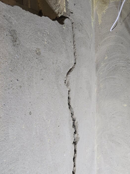 Vägg med spricka och frilagd murbruksyta, förberedd för eldragning och lagning i en renoveringsmiljö.