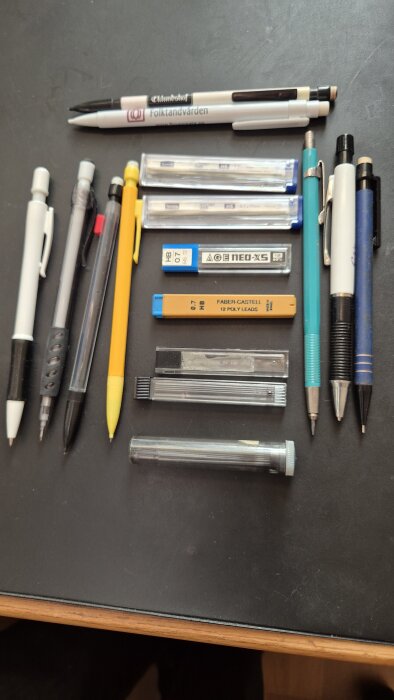 Olika stiftpennor och behållare med stift i olika färger ligger på ett bord.