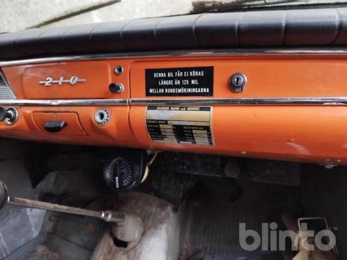 Instrumentpanel i en orange gammal bil med text om serviceintervall och ett emblem som visar "210".