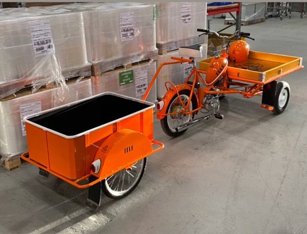 Orange flakmoped från 60-talet med sidovagn i lagerlokal, står bredvid staplade kartonger.