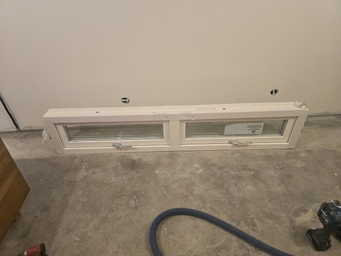 Liggande fönster med två handtag placerat på golvet i ett rum under renovering.
