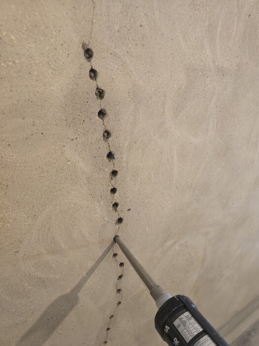 Spricklagning i vägg med tätningsmedel, flera borrhål synliga längs sprickan.