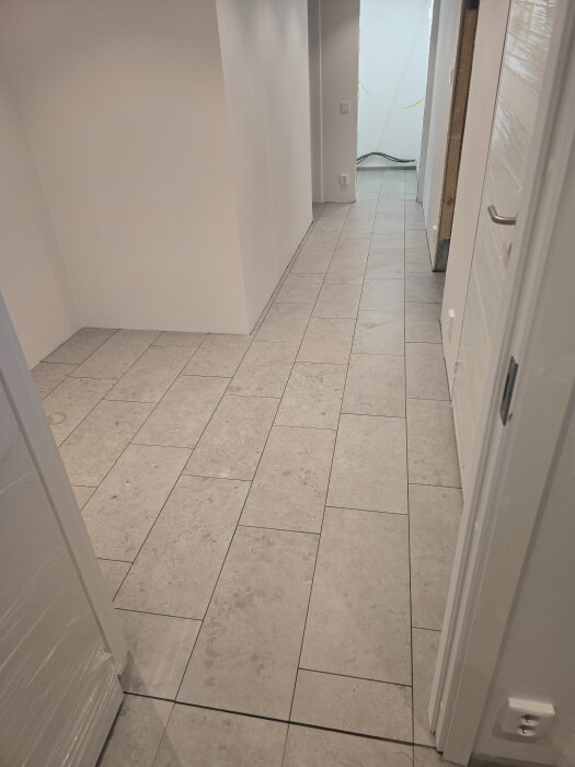 Korridor med nylagt klinkergolv och vita väggar. Plattsättning med längsgående fogar. Rummet färdigställt inför fönsterbyte.