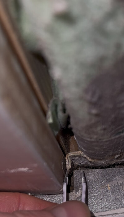 Närbild på våtrumstätskikt som inte är korrekt installerat vid dörrtröskel, med en hand som pekar på felet.