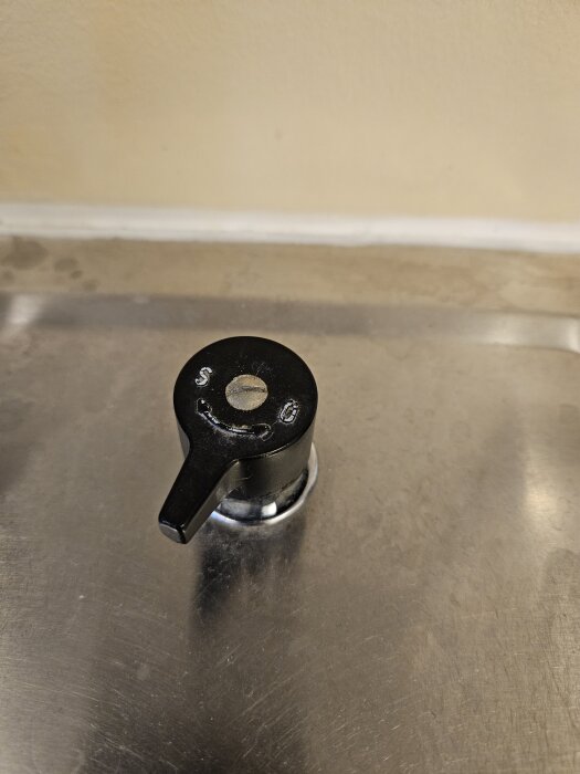 Svart avstängningsventil med handtag på en metallisk yta, del av tvättmaskinsinstallation.