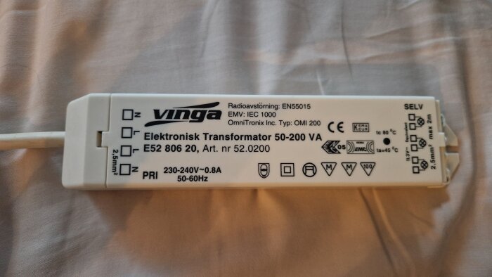 Elektronisk transformator av märket Vinga, modell OMI 200, 50-200 VA, med specifikationer och symboler synliga på en ljus bakgrund.