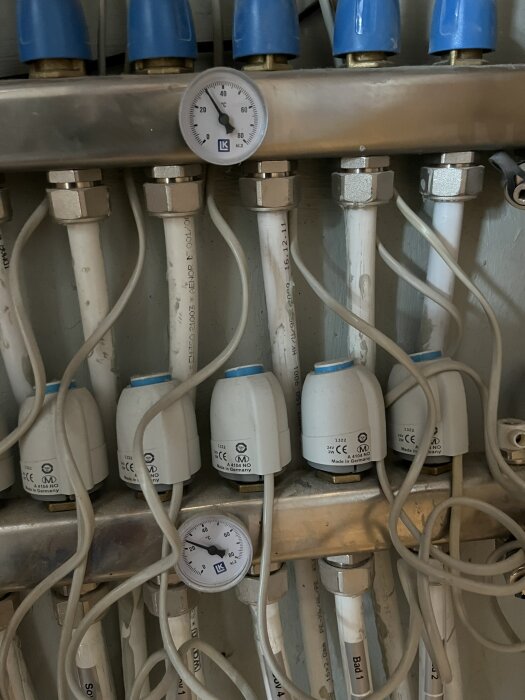 Värmefördelare med termometrar och vita ventiler, sammankopplade med rör.