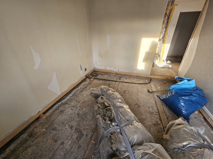 Rivet sutteränghus med blottad betongplatta och golvreglar borttagna. Byggmaterial i plastpåsar och verktyg synligt i rummet.