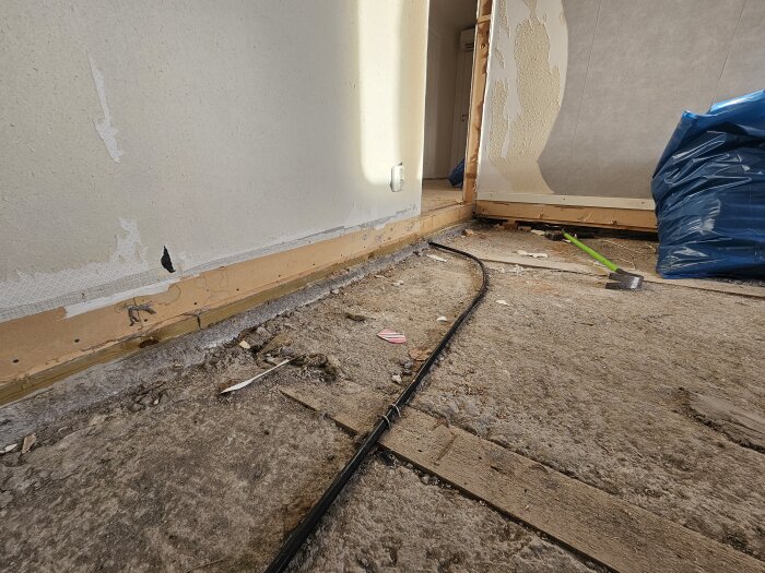 Betonggolv i sutteränghus med borttagna spikreglar, lösa verktyg och en sophög, väggar delvis rivna och elsladd ligger synlig.