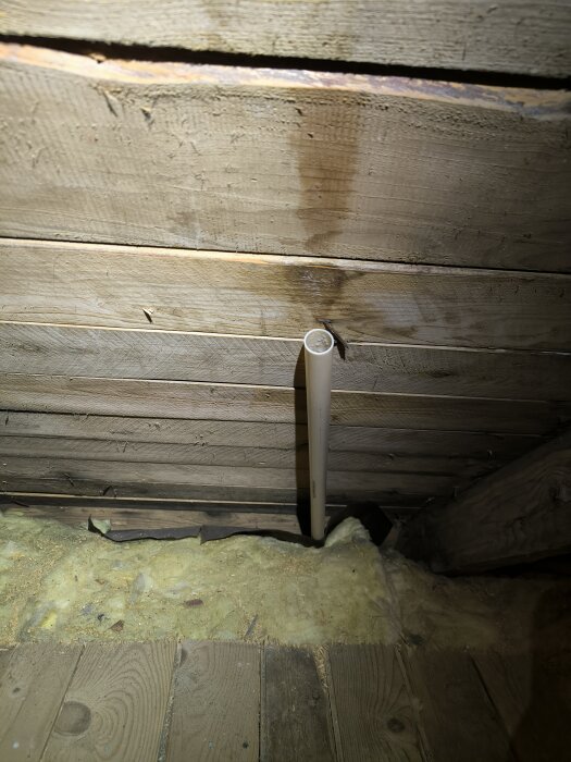 Rörstump av plast som sticker upp från taket på en kallvind med synlig fuktfläck på träets yta. Huset är från 1930-talet.