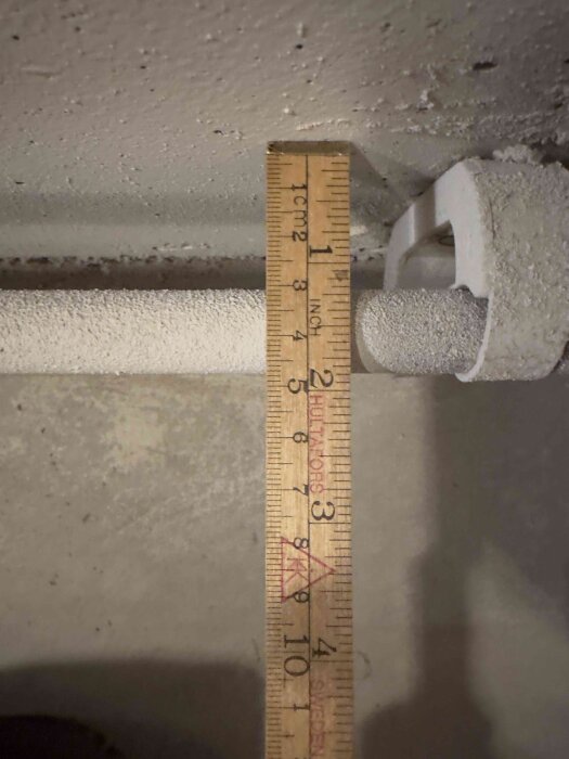 Måttstock mäter avstånd från vägg till rör i renoveringsprojekt.