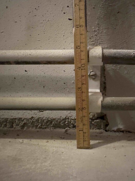 Linjal mäter avståndet från vägg till två rör, monterade horisontellt med klämmor, i en betongvägg i kök.