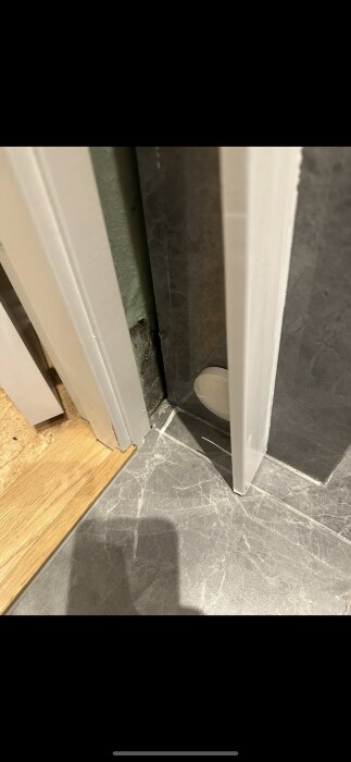 Dörrkarm vid tröskel med synligt mellanrum, visar hur vatten kan tränga in. Golvet är av grå plattor och väggen har felaktigt dörrfoder.