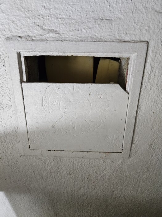 Luftintag i betongvägg med vit metallram och lucka delvis öppen, inuti finns skumgummi som temporär fyllning vid ombyggnad till badrum.