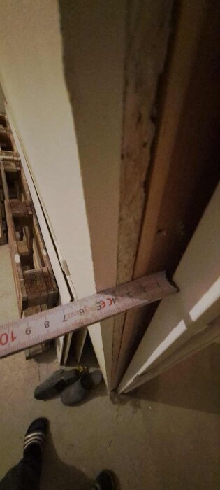 Mätning av 6-10 mm spalt vid gipskant nära fönster, med fötter och skor synliga på golvet.
