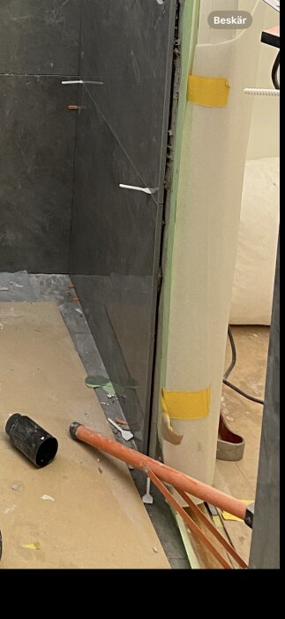 Vattenläckage vid kakelvägg med vikt tätskiktsflik och pincett; orange plast och svart rör på golvet.