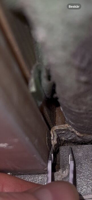 Närbild av en tröskel med en felvikt tätskiktsflik intill pincett, där vatten trängt in.