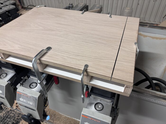 Bearbetning av träpanel fäst med klämmor på arbetsbänk, med snitt längs fiberriktningen, i en verkstadsmiljö.