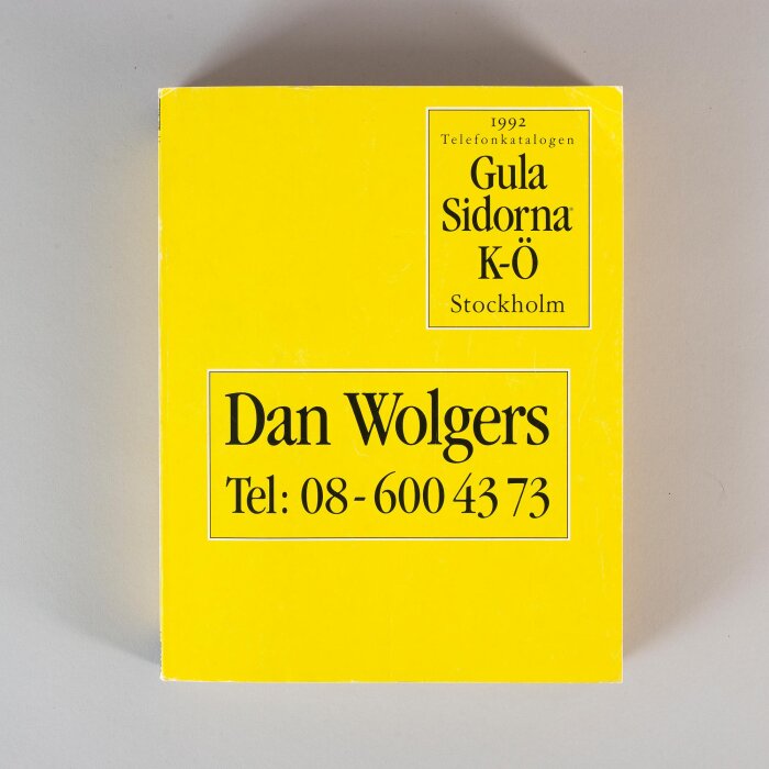 Telefonkatalog från 1992 med gul framsida formgiven av Dan Wolgers, innehåller texten ”Gula Sidorna K-Ö Stockholm” och hans telefonnummer.