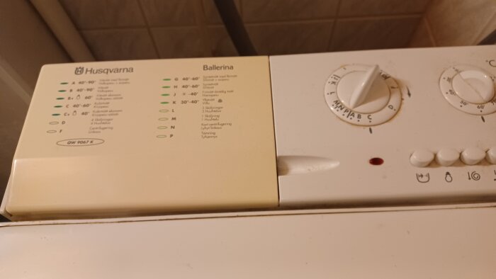 Tvättmaskin av märket Husqvarna Ballerina med panel och olika tvättprogram bredvid en knapp och ratt för inställningar.