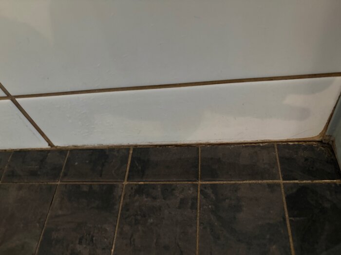 Fog mellan kaklade vägg- och golvplattor i dusch som har lossnat, vilket antyder att reparation behövs.