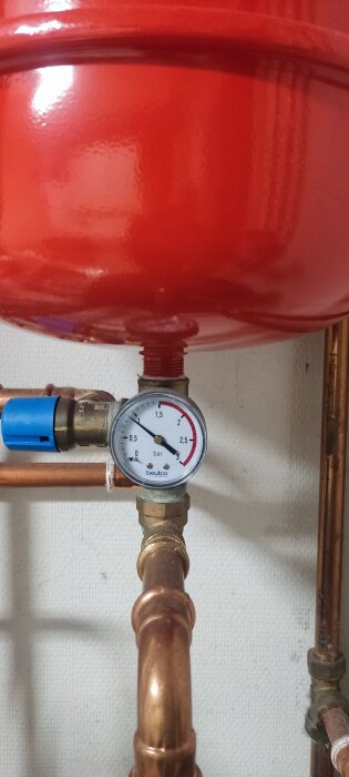 Tryckmätare monterad på kopparrör med anslutning till en röd expansionskärl i ett värmesystem.