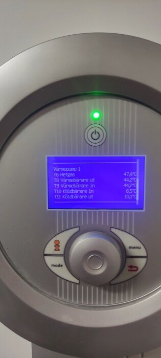 Närbild av en värmepumpskontrollpanel med blått LCD-skärm som visar temperaturvärden; en grön lampa lyser.