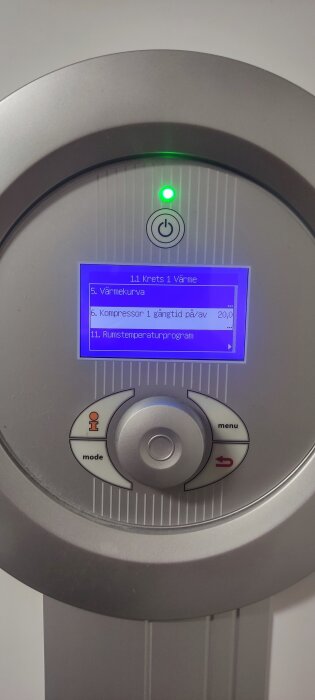 Närbild av en värmepumps kontrollpanel med en digital skärm som visar inställningar för rumstemperatur och kompressor.