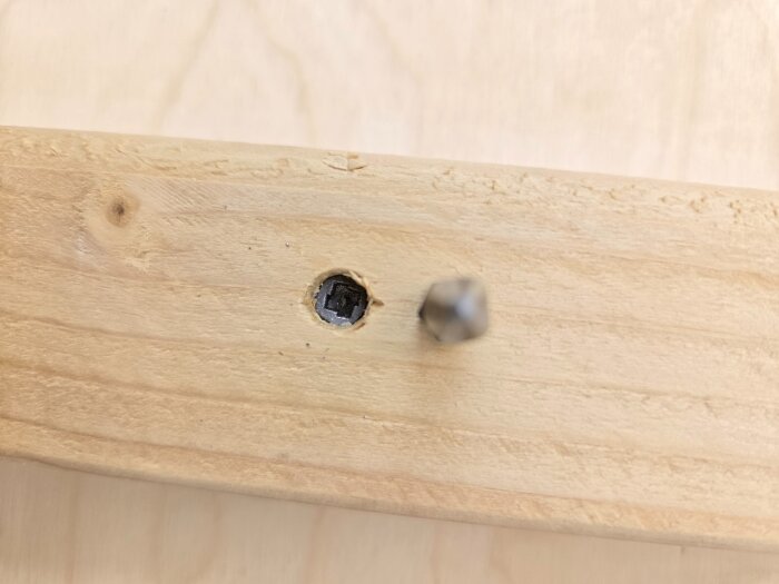 Närbild av träregel med ovanlig skruv, PH2-bits ligger bredvid för storleksjämförelse.