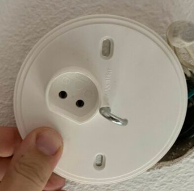 Rund vit takdosa med krok och två hål, hålls av en hand.