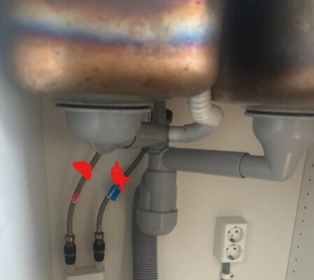 Under diskbänk med två synliga vattenrör och silar. Två slangar från blandaren, ingen tredje synlig.