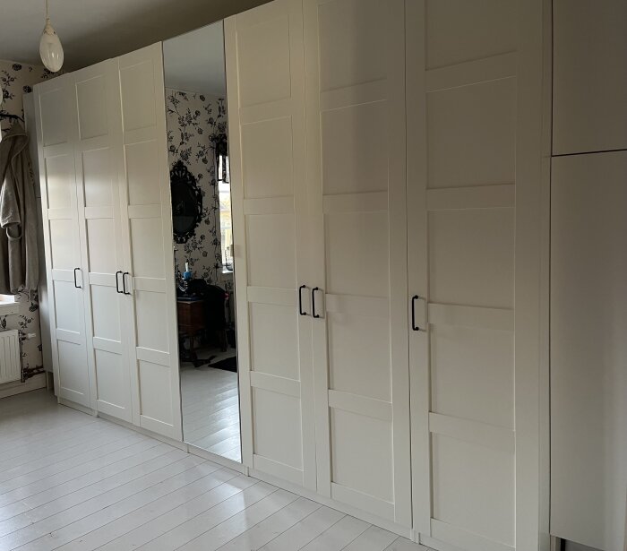 En rad vita garderober med nyinstallerade svarta handtag, varav en garderobsdörr har en spegel.