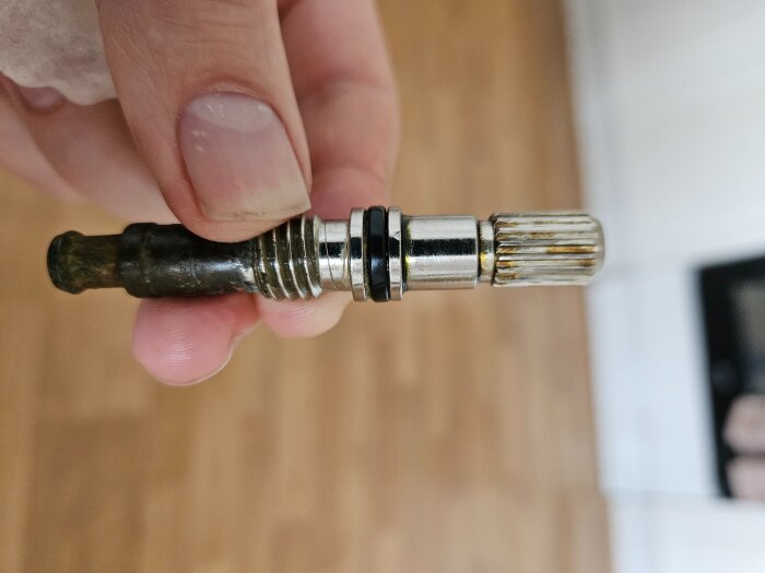 En hand håller en metallkomponent med gängor och räfflad topp, troligen en del av ett bygg- eller renoveringsprojekt.